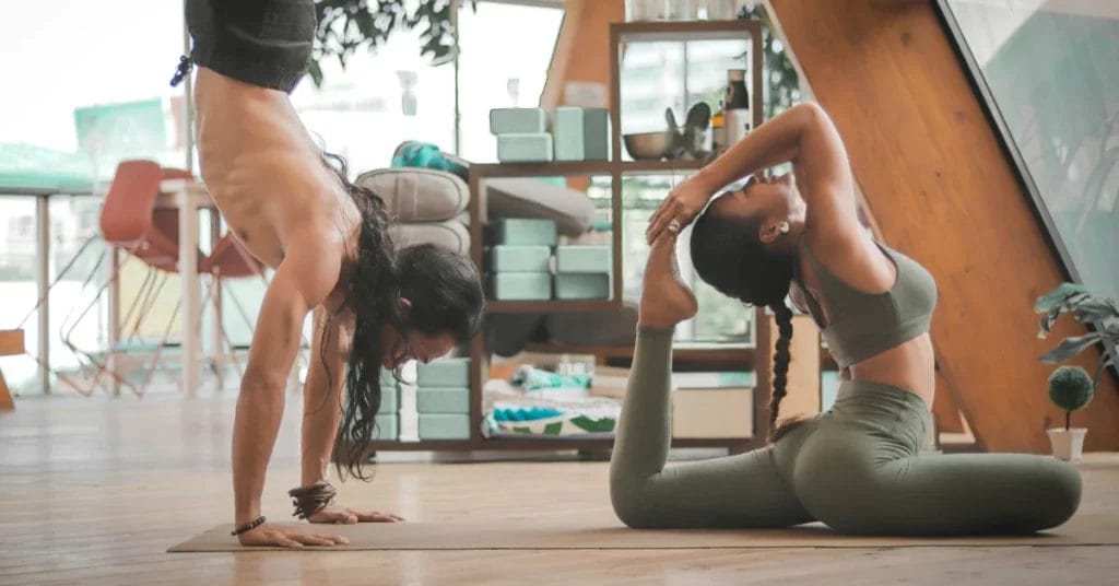 A couple in a home living room sharing a yoga mat doing yoga poses