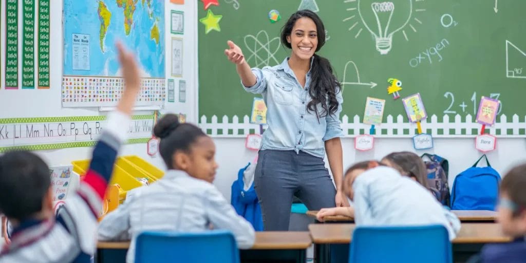 Teacher in a classroom setting with a student raising their hand.