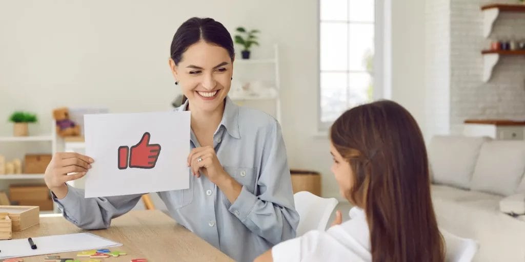 A tutor holds up an icon of a "thumbs up" to a student