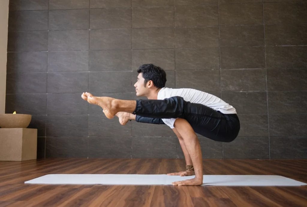 Side view of a male yogi performing firefly pose in front of a dark wall.