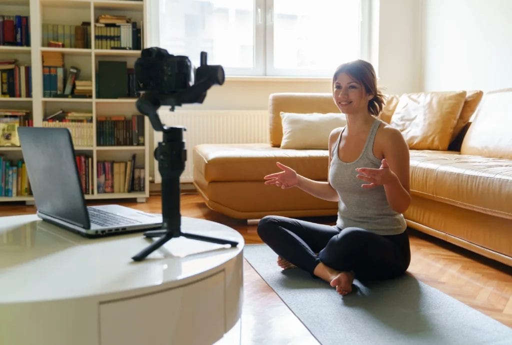 A yogi sits in a living room speaking to the camera while filming.