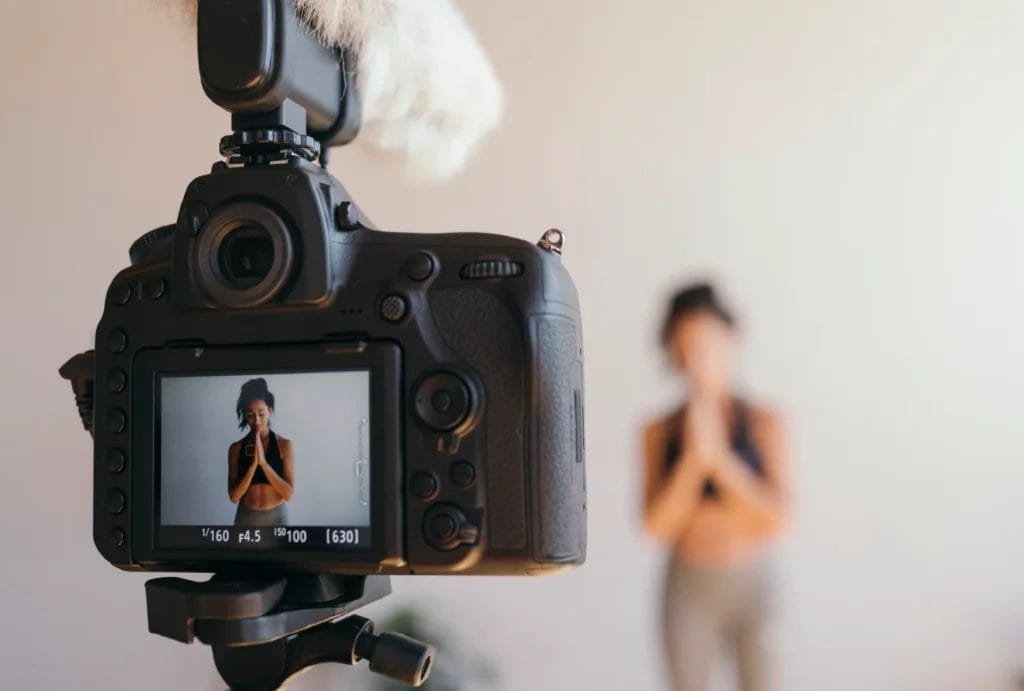 Close-up of a video camera recording a yogi in a standing position with hands at heart center.