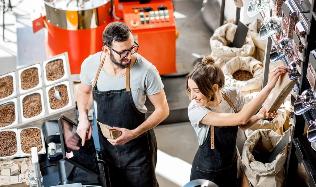 Two workers are packaging coffee beans in a warehouse together as they prepare customer orders.