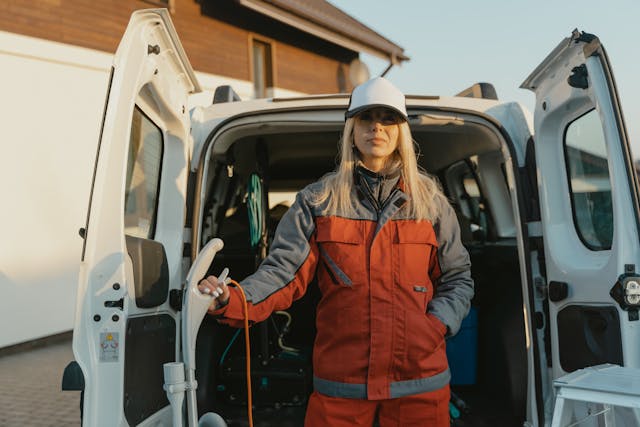 a uniformed woman holding a vacuum stands in front of a cleaning truck