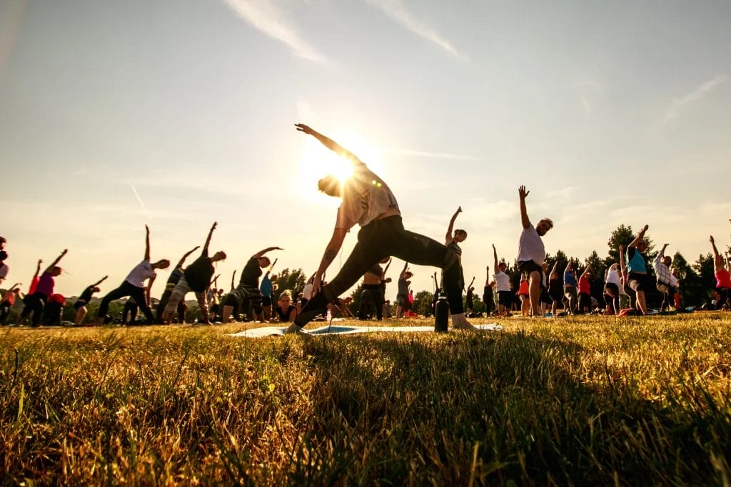 A large outdoor yoga with people stretching in warrior pose as the sun sets, creating a serene atmosphere in an open field.