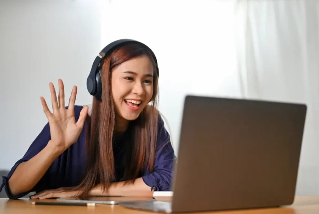 A virtual tutor waves hello to a student through her laptop as she starts a session.