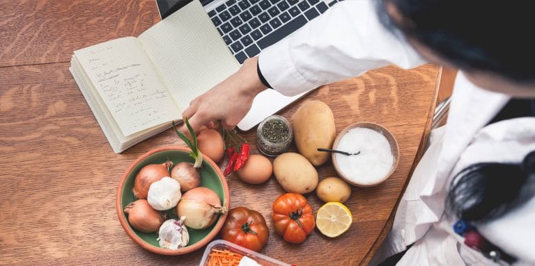 A dietician with assorted foods on a table by a laptop.