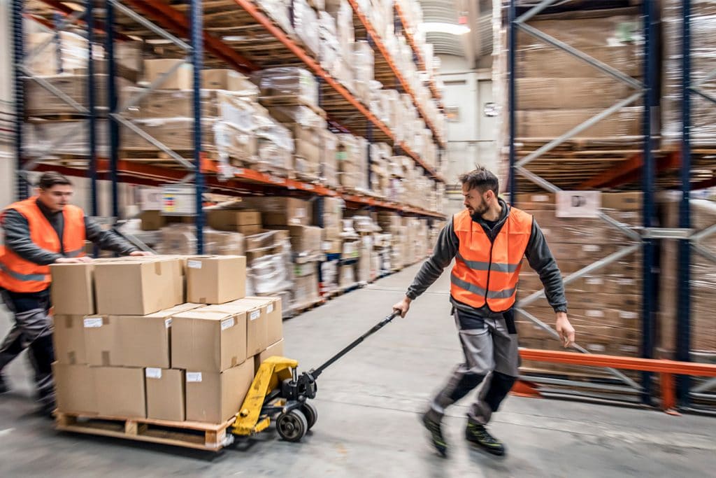 Workers quickly pull a pallet of boxes across a warehouse.