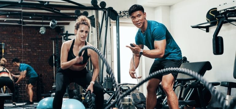 A fitness instructor helps train a client with battle ropes.