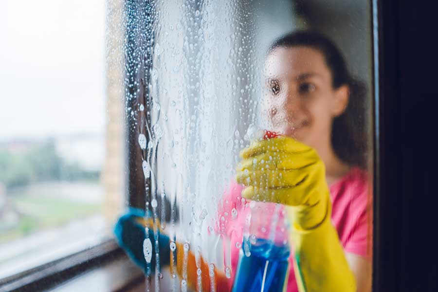 woman cleaning window with windex