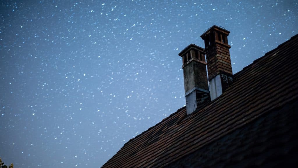 A chimney on a roof in front of a starry sky.