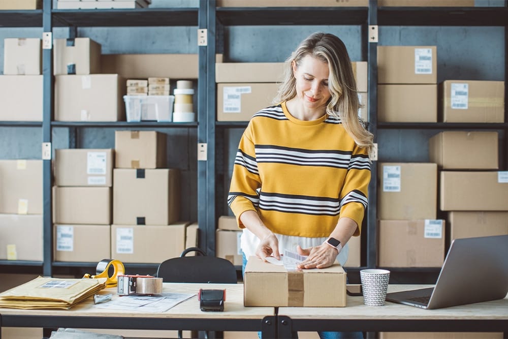 a small business owner packs products into a box for shipping.