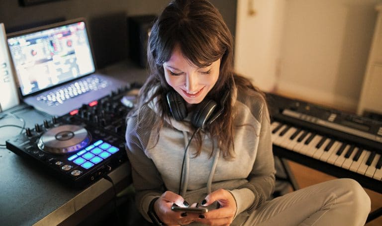 woman with turntable and computer looking at her phone