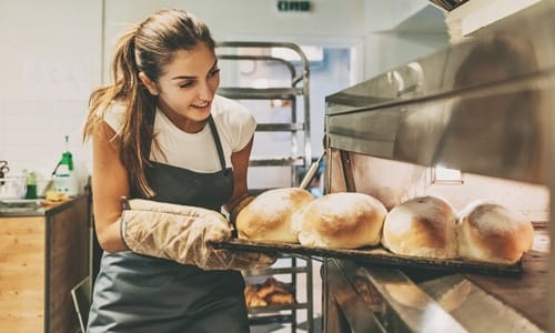 baker pulling loaves of bread out of oven