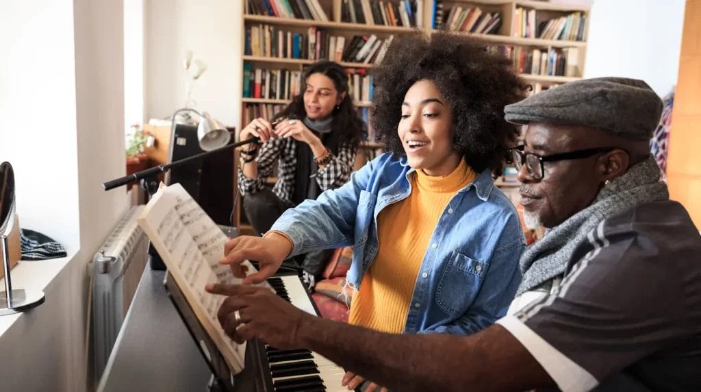 Music teacher going over sheet music with a student seated at a piano.