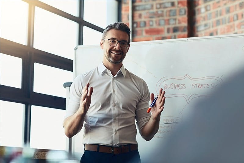 A man details a marketing strategy with a whiteboard.