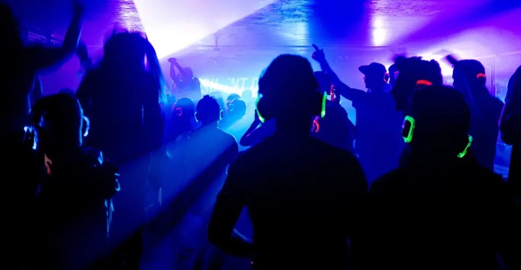 People at a silent disco party wearing headphones and dancing.