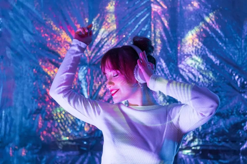 Person at a silent disco party wearing headphones and dancing in front of a metallic background.