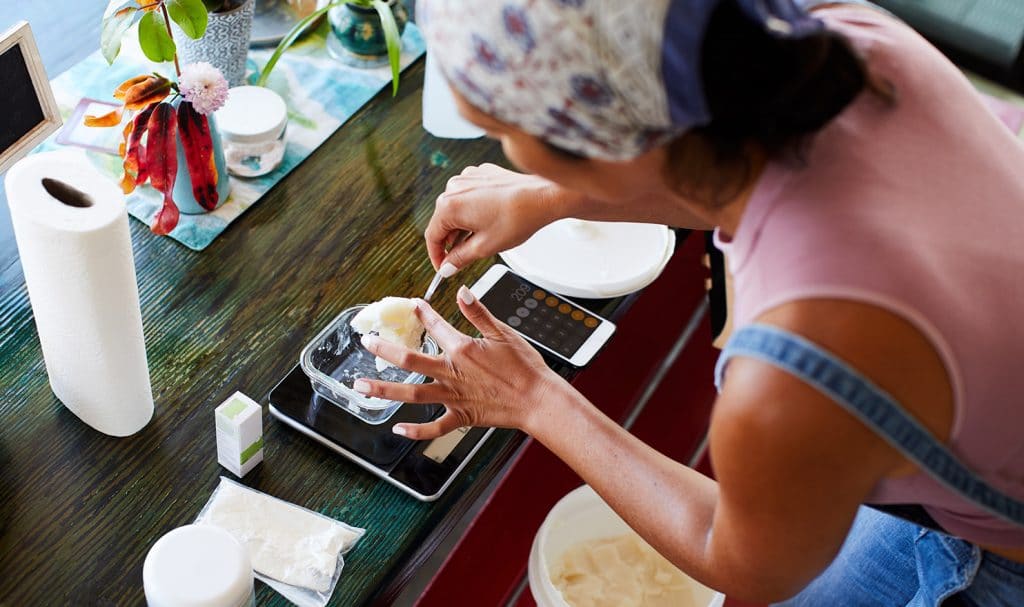 A women leans over a table where she is making homemade beauty supplies and pricing her product.