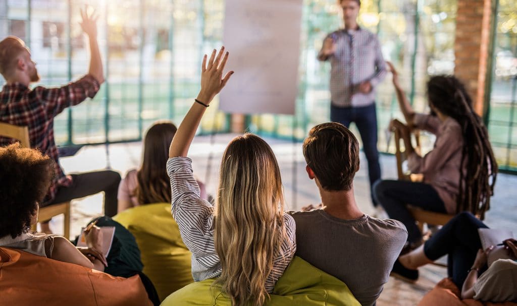 A group of people participate in a focus group and a women is raising her hand to answer a question.