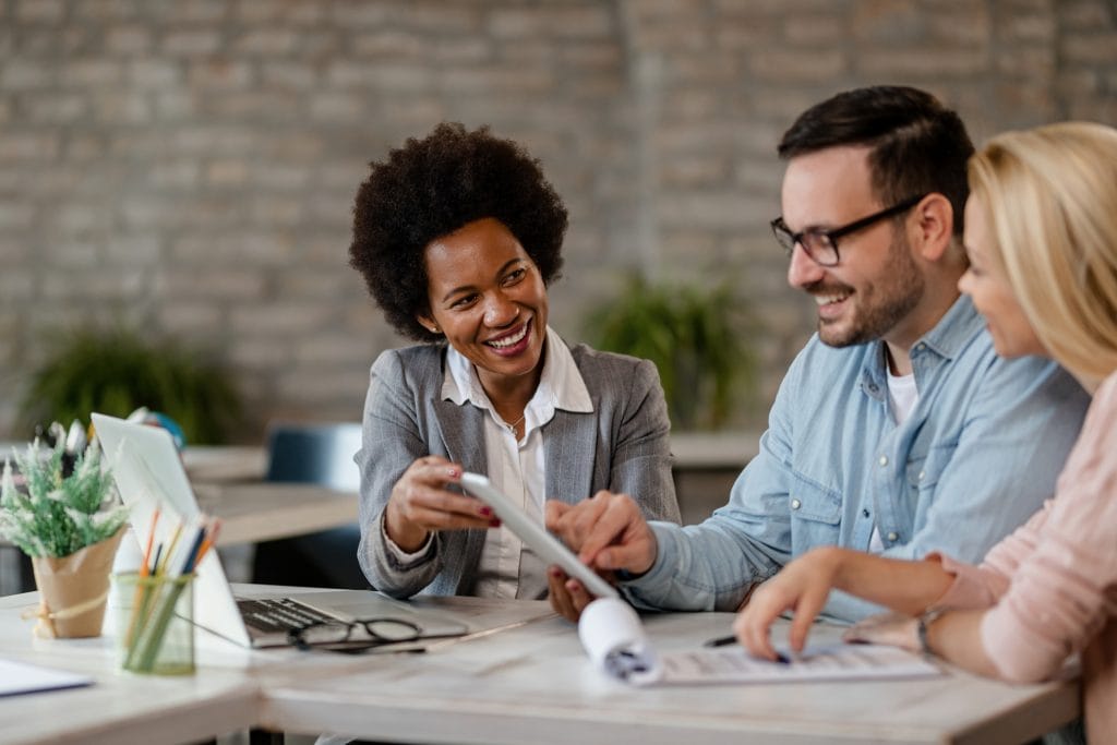 Happy auditor and a couple using digital tablet during a meeting in the office.