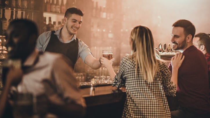 A gathering of people at a bar with a bartender attending to their orders in the background.