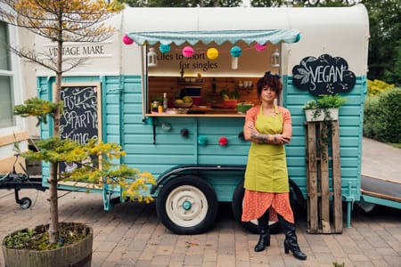 A food truck owner proudly poses in front of her truck decorated for an event.