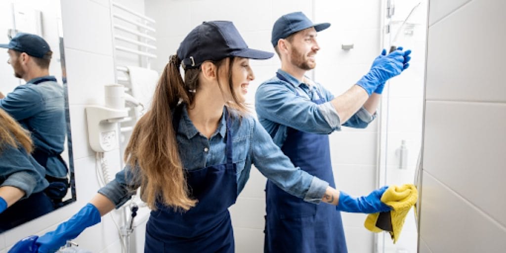 smiling man and woman cleaning a bathroom with blue rubber gloves on