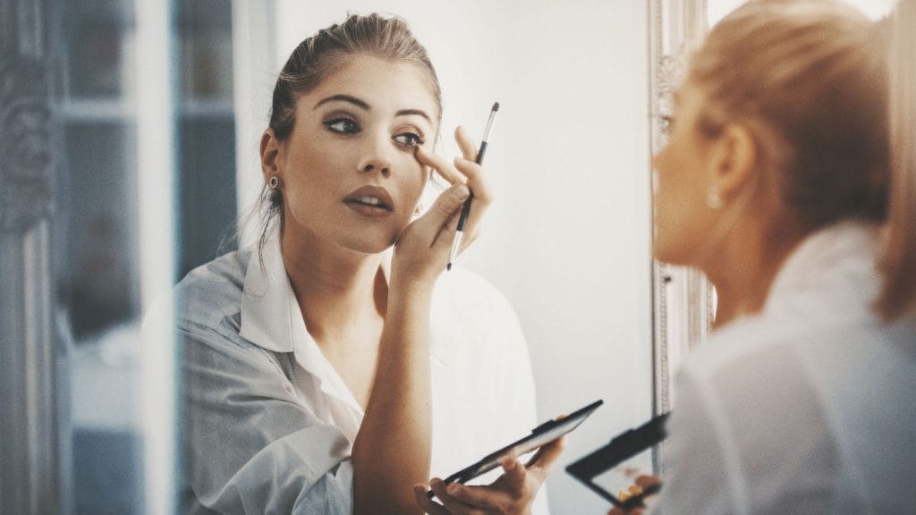 A woman applies makeup in a mirror.
