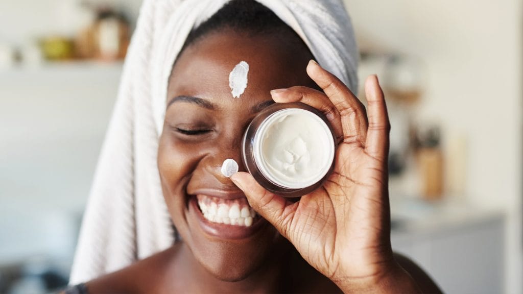 a woman holds up a facial cream with a smile.