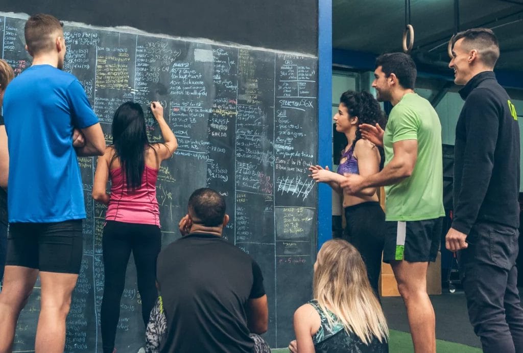 a group of people around a black board planning a workout at a crossfit gym