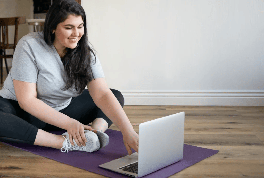 A woman in the butterfly stretching pose watching her laptop