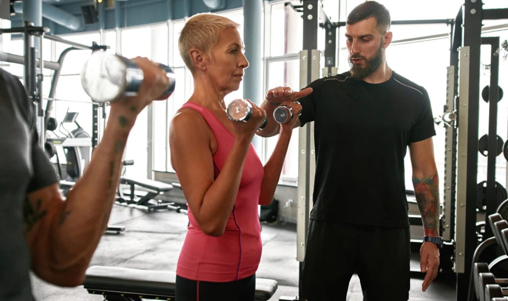 Personal trainer adjusting a workout to fit an older client.