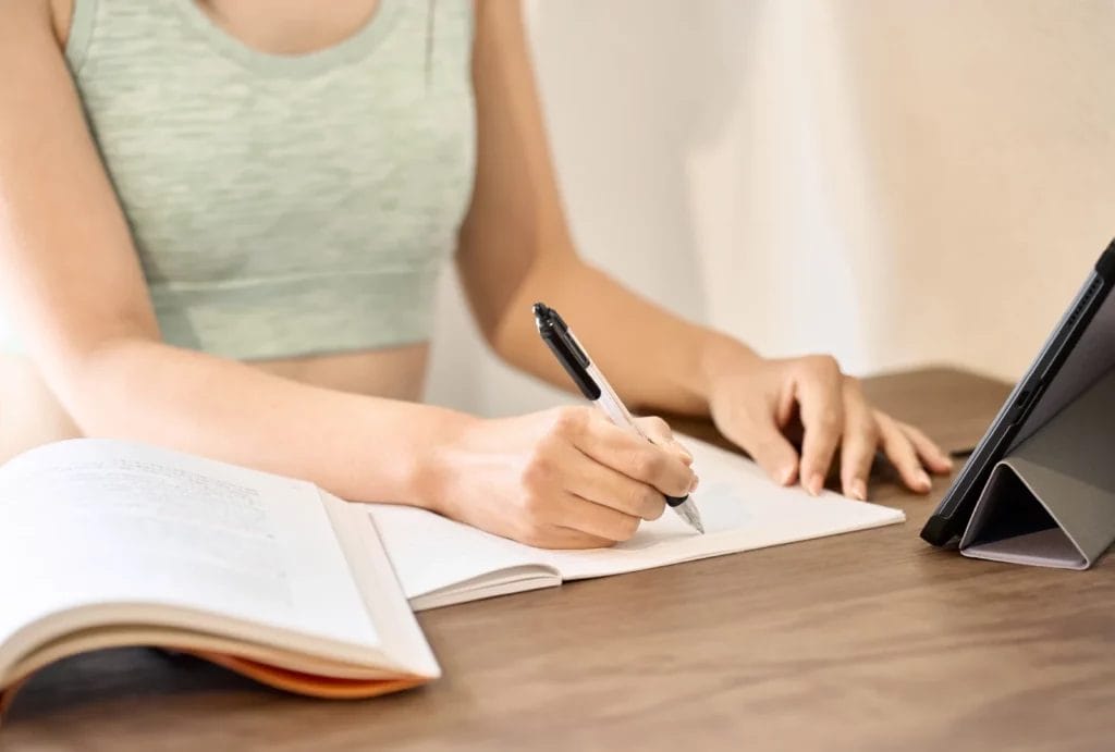 Woman in light green sports bra studying a textbook and taking notes.