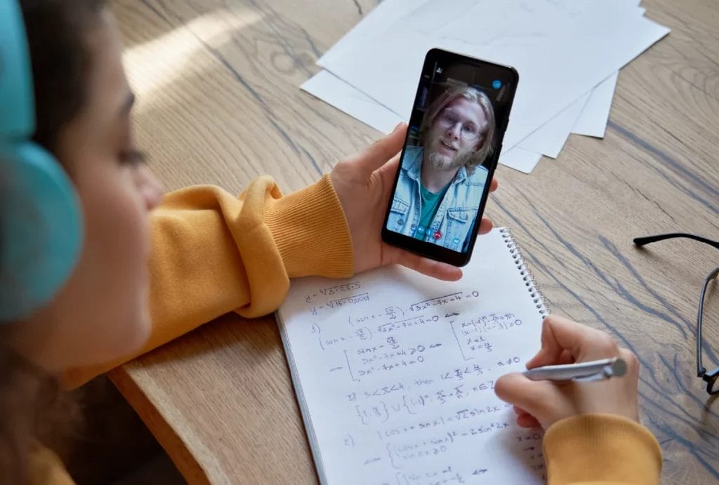 Student holding phone and doing a math problem while on a call with an online tutor