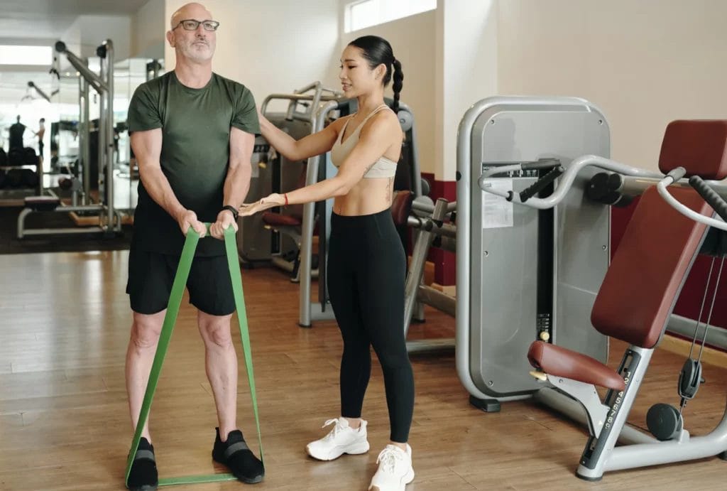 A female personal trainer assisting an older man practice curls using a stretch band