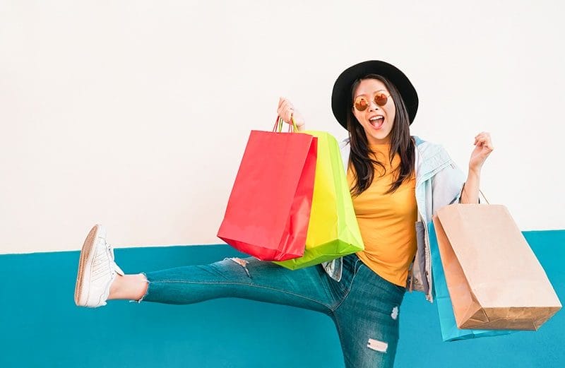 A woman smiles with a several bags of products.