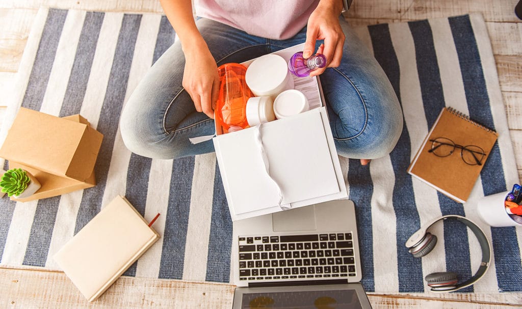 An individual is sitting with their legs crossed on the ground as they look over the different items going into a shipment. If these items are damaged in shipping on their way to the customer, product liability insurance may be able to help cover these costs.