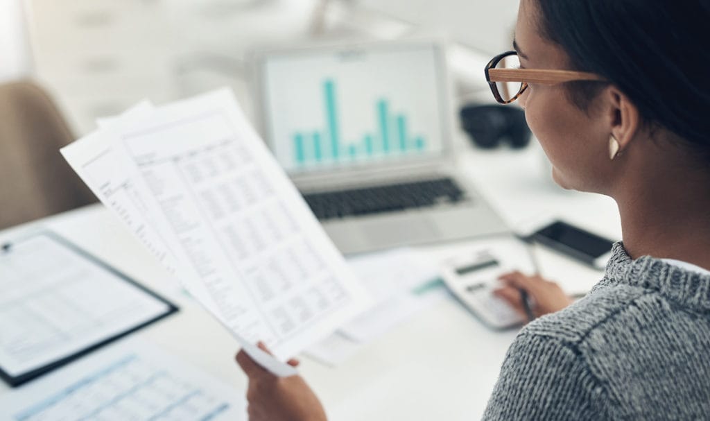 A woman is comparing her business documents with information online as she applies for a cheap product liability insurance quote.