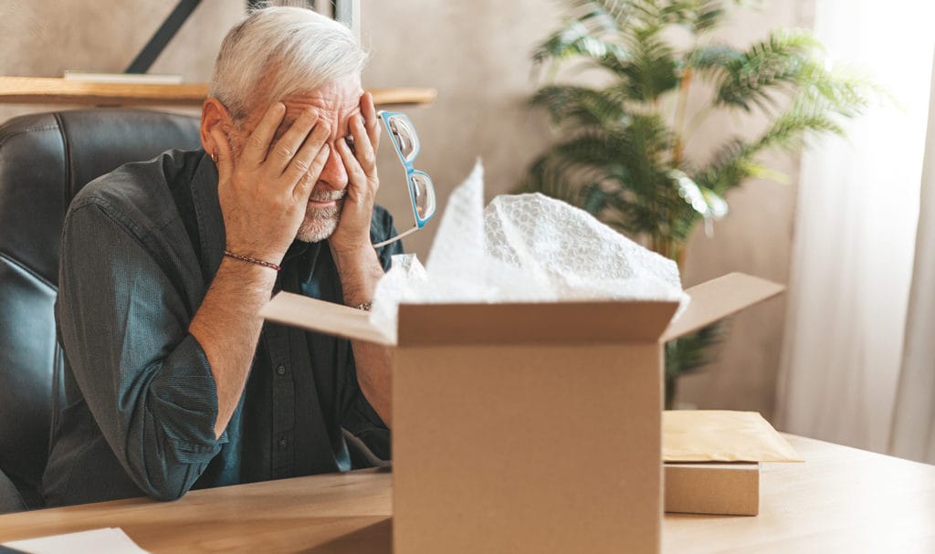 A man is upset at his desk at a damaged product in a box. Product liability insurance may cover an incident like this.