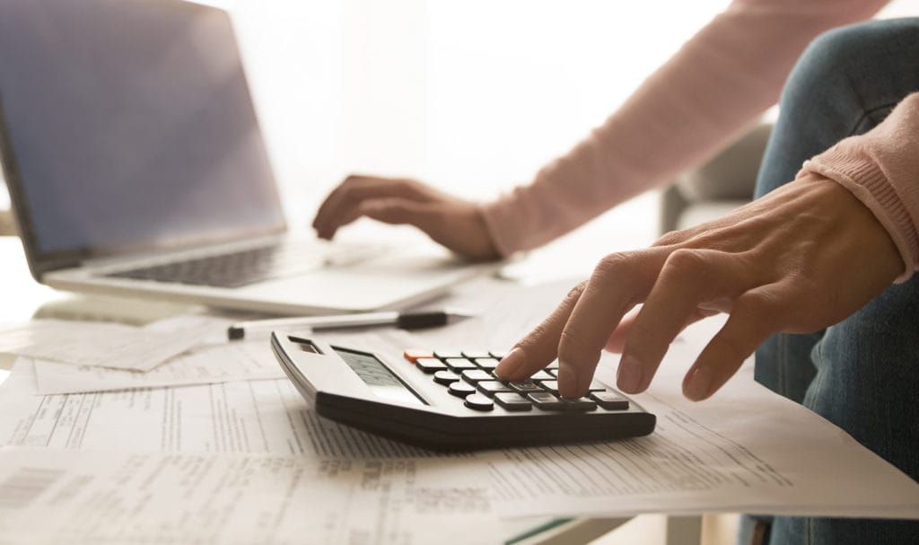 A pair of hands are working on a laptop and a calculator someone is using to buy product liability insurance.