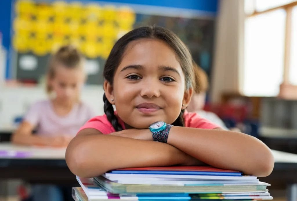 Young student in classroom resting her chin on a stack of books