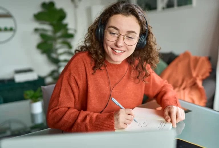 Online student or tutor wearing headphones and writing notes