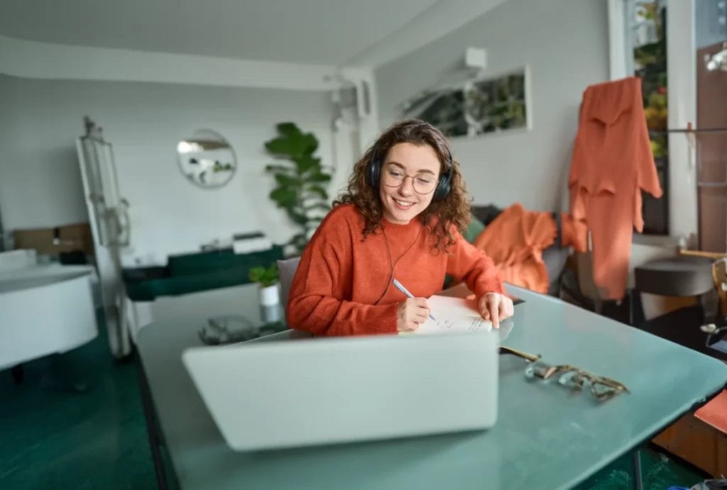 Online student or tutor wearing headphones and writing notes