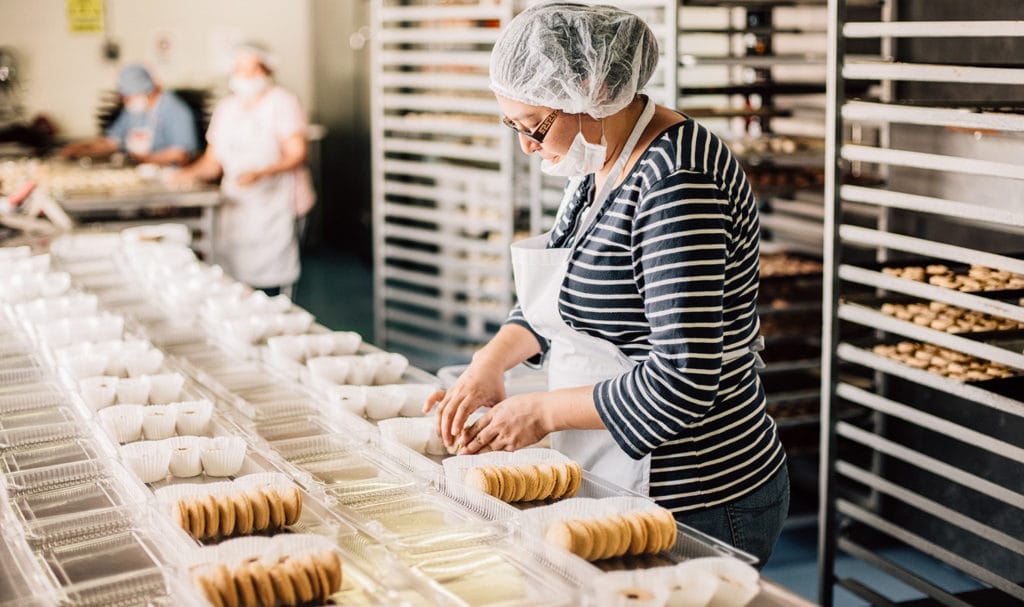 A woman is packaging food into containers. This kind of work could be protected with food manufacturers insurance.