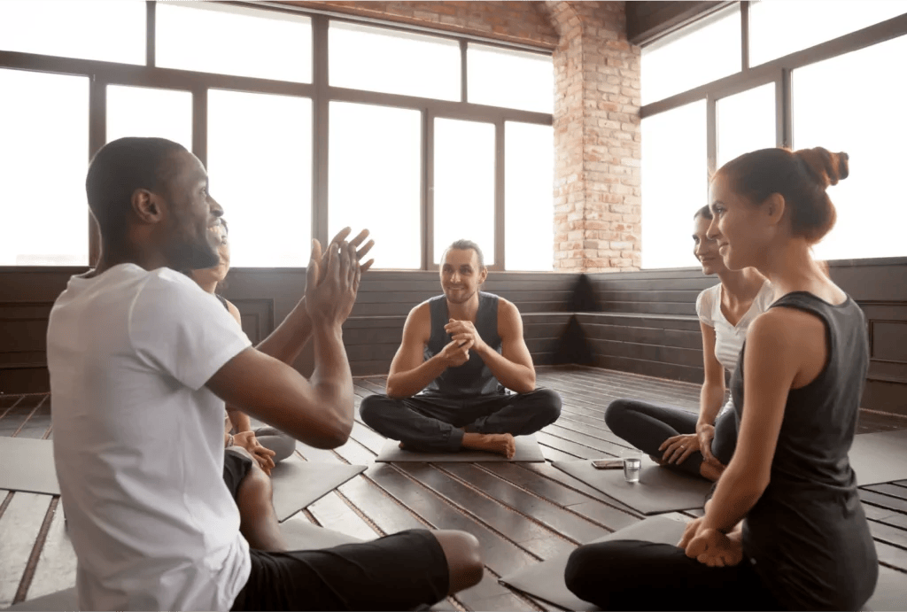 A group of yoga teacher candidates sit in a circle in a studio.