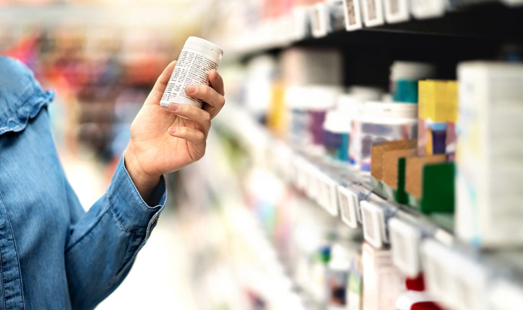 A person is pulling a bottle of medication off a store shelf and reading the label. If the product was tampered with, product liability insurance may be able to help cover the cost of claims.