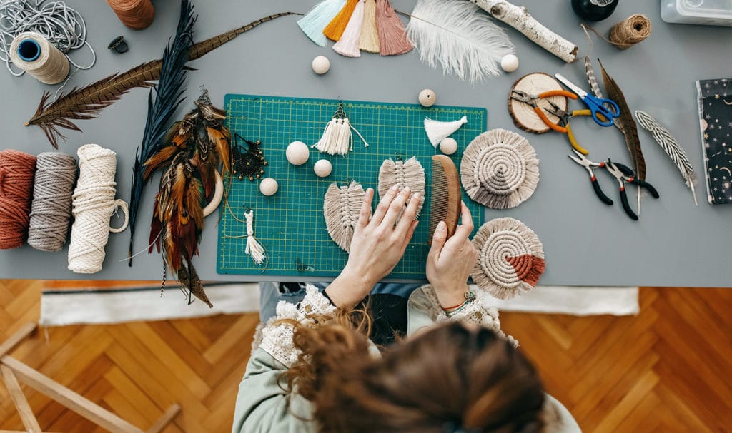 A handmade jeweler is creating sets of earrings at her crafting table.