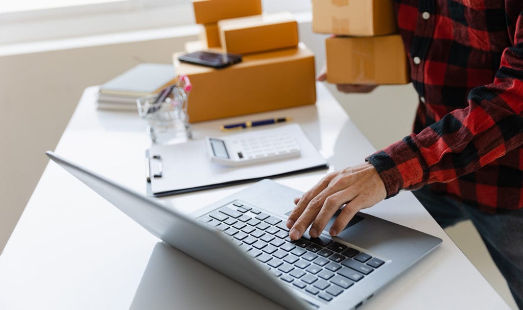 A man holds packages while using a computer as he researches the best product liability insurance.