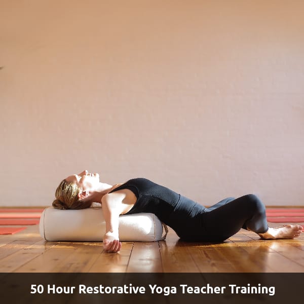 A yoga teacher stretches on a tall pillow. Text Reads: 50 Hour Restorative Yoga Teacher Training.